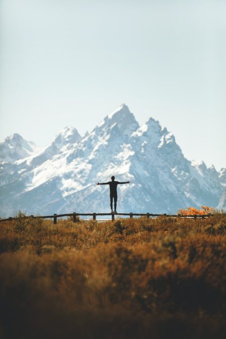 man standing on fence overlooking mountain in backcountry